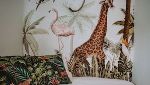A bedroom with a mural of a giraffe, flamingo, and leopard, and a jungle-themed pillow.