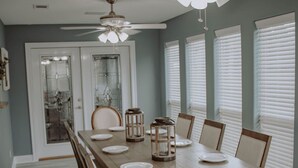 A dining room with a large wooden table, white chairs, and two ceiling fans.