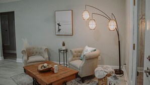 A living room with a wooden coffee table, two armchairs, a floor lamp, and a framed picture on the wall.