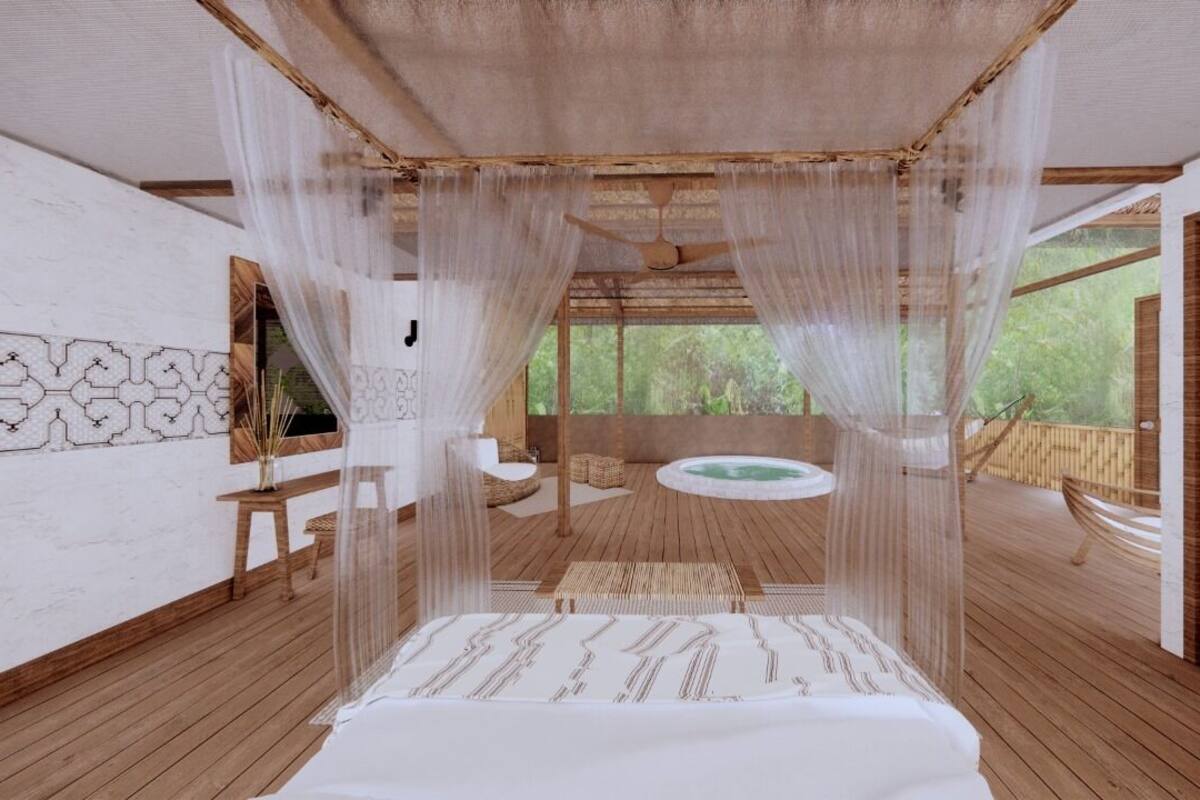 A room with a bed, a small table, and a bench. There is a window with a view of greenery outside.