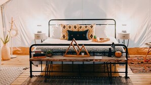 A tented room with a bed, two bedside tables, a bench, and a small table with a plant. - Deluxe Safari Tent Glamping at Unicoi in Helen GA - 15 (Helen)