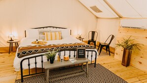Una habitación tipo tienda de campaña acogedora, con cama, mesitas de noche, una pequeña mesa, sillas y una planta en maceta.