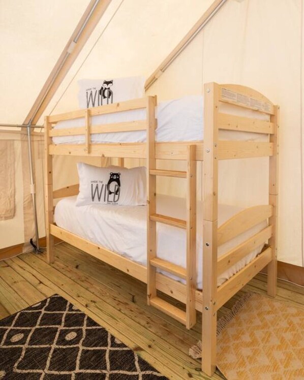 Una litera con dos almohadas, una con diseño de oso, en una habitación tipo tienda con suelo de madera.