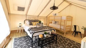 Een tent met een bed, een stapelbed, een kleine tafel met een lamp en een hangende lamp.