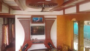 Quarto com televisão na parede, ventoinha no teto e janela com cortinas.