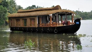Uma casa flutuante com telhado de palha, paredes de madeira e área de deck coberta.