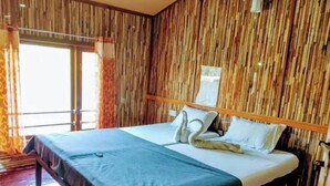 Quarto de hotel com cama, painéis de madeira na parede e uma janela com cortinas.