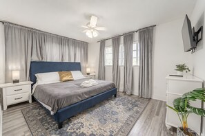 A bedroom with a bed, nightstands, a desk, a TV, and a plant. - 2 BD Condo - Sleeps 4 - Palm Wave Stays (Coconut Creek)