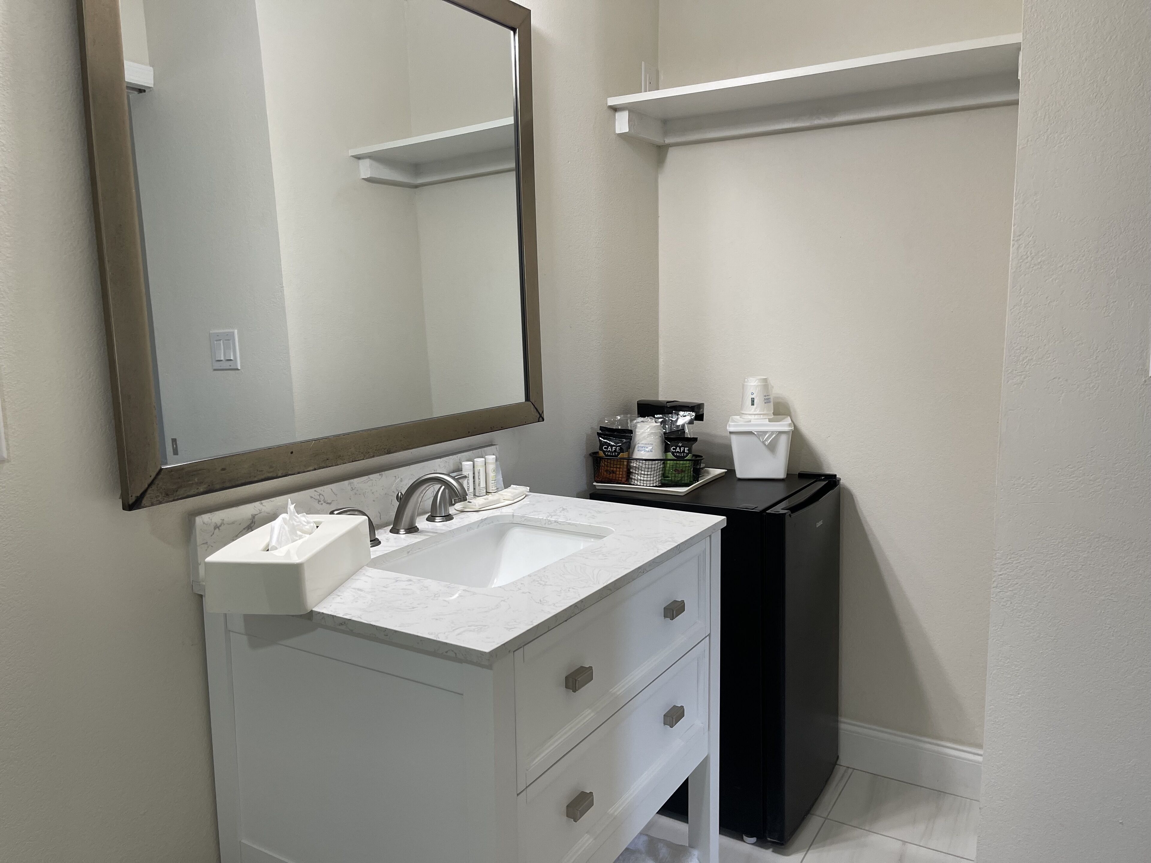 A bathroom with a white sink, a mirror, a black cabinet, and a coffee maker.