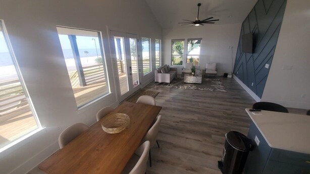 A spacious living area with a wooden dining table, white chairs, and a large window overlooking a beach. - Family-Friendly! (Gulfport)