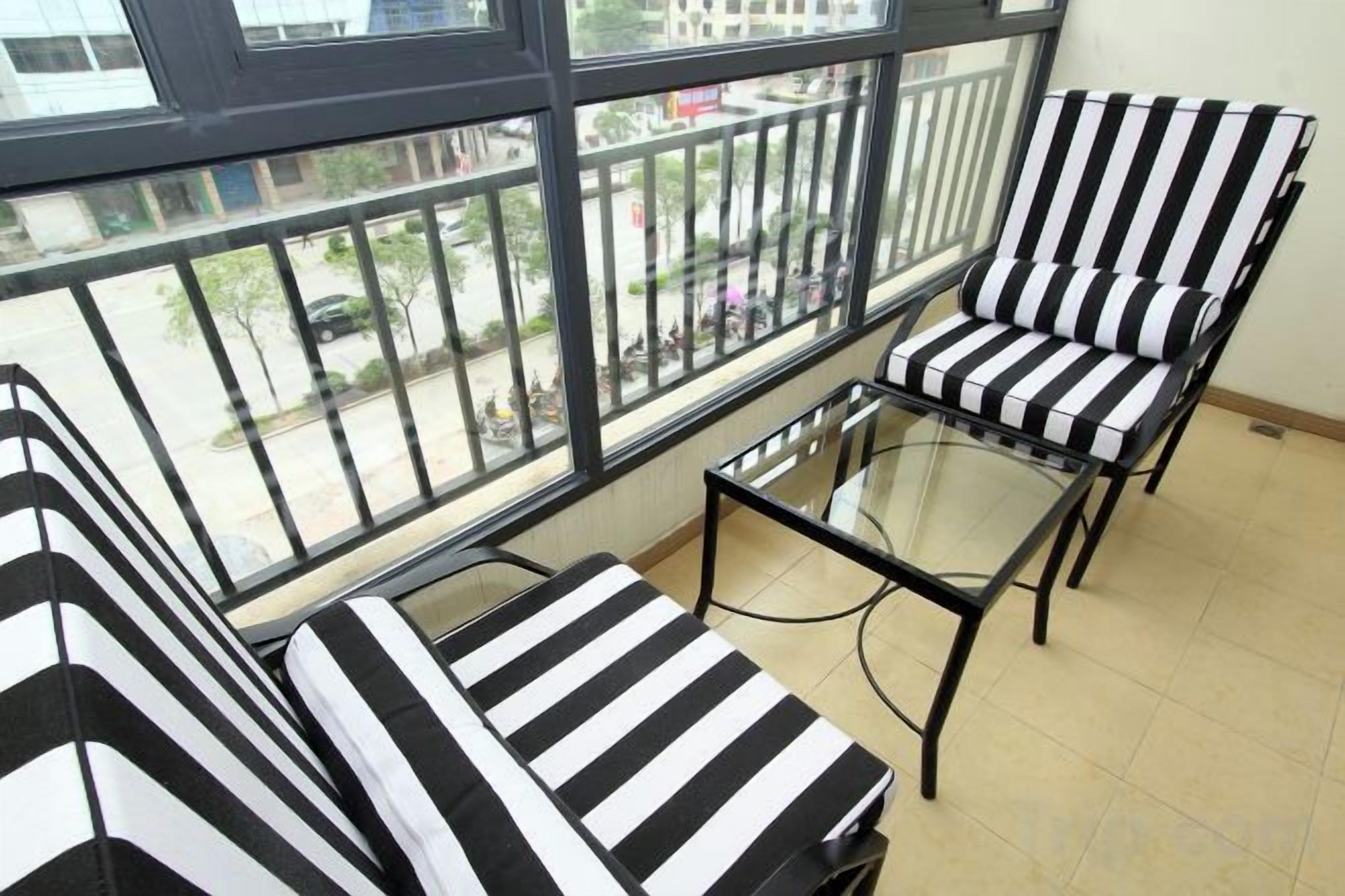 A balcony with striped chairs and a glass table, overlooking a street.