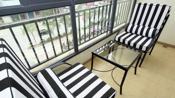 A balcony with striped chairs and a glass table, overlooking a street.