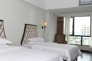A hotel room with two beds, a lamp, and a view of buildings through large windows. - Zhonghui Hotel (Lingchuan)