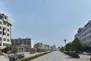 A multi-story building with a flat facade, a clear sky, and a road with parked cars. - Zhonghui Hotel (Lingchuan)