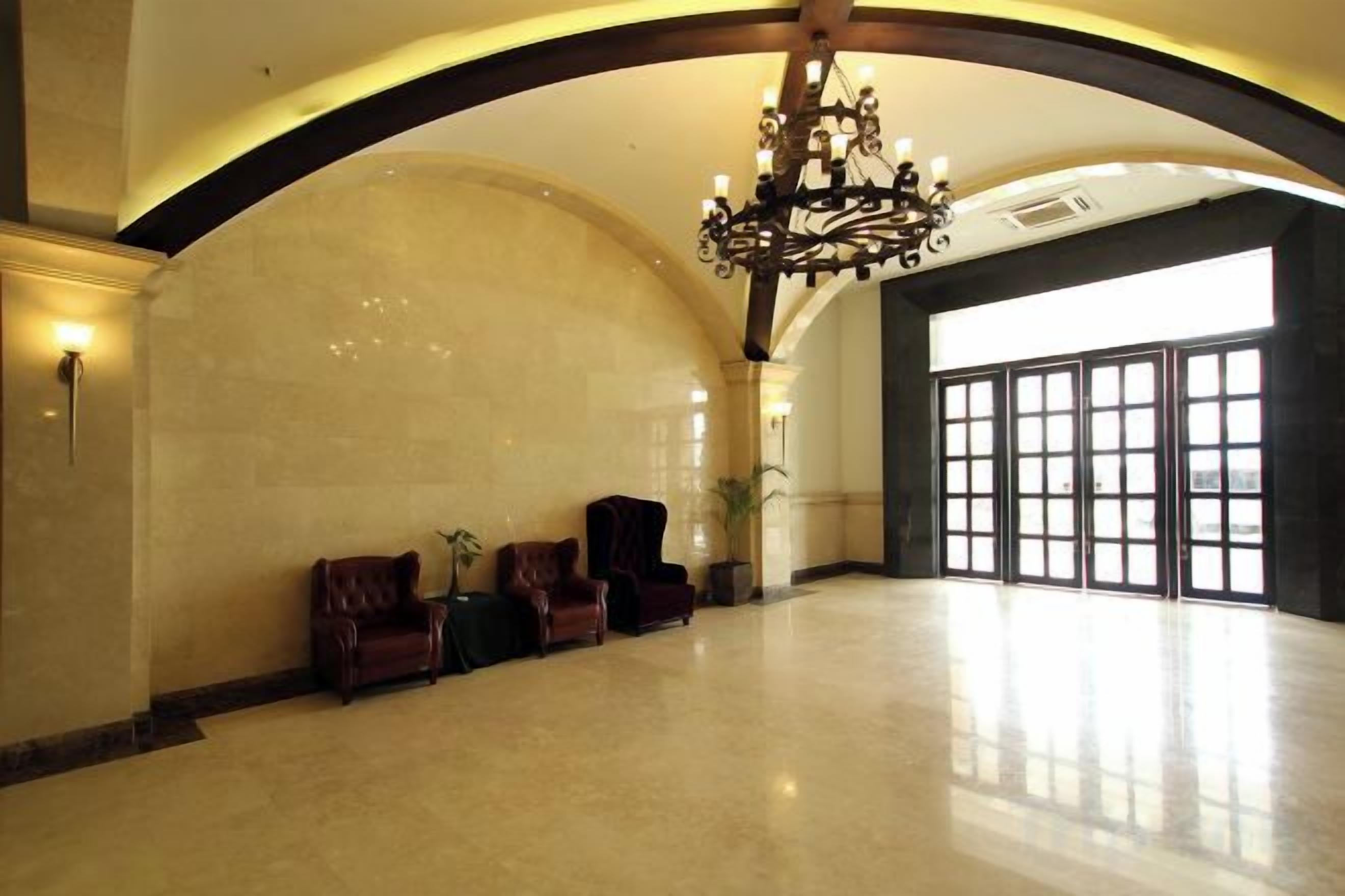 Un hall d’entrée spacieux avec un plafond haut, un lustre et un coin salon doté de fauteuils en cuir.