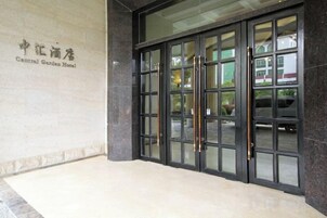 Entrada de hotel con puerta de vidrio, un cartel sobre la puerta y un camino pavimentado que conduce a la entrada.