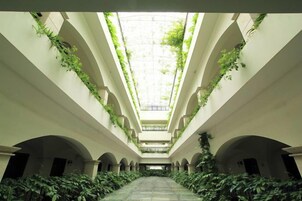 Un largo pasillo con arcos y vegetación creciendo en las paredes, que conduce a un espacio central abierto.
