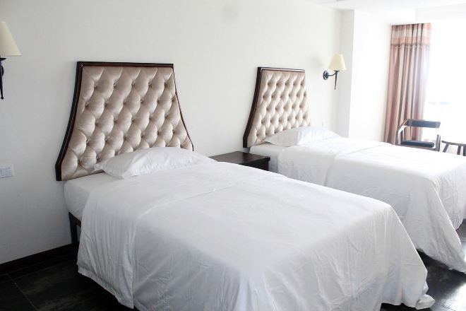 Een hotelkamer met twee bedden, elk met een gebosterd hoofdeinde, witte beddengoed en een nachtkastje met een lamp.
