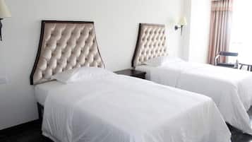 Een hotelkamer met twee bedden, elk met een gebosterd hoofdeinde, witte beddengoed en een nachtkastje met een lamp.