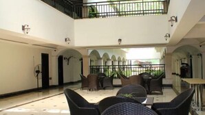 A spacious indoor area with a high ceiling, featuring a central seating area with chairs and tables, surrounded by arches and a glass railing overlooking a garden. - Zhonghui Hotel (Lingchuan)