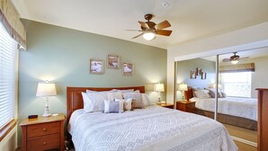 Una camera da letto con un letto grande, due comodini con lampade, una ventola a soffitto e tre quadri appesi al muro.
