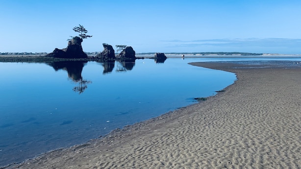 Una spiaggia con acque calme, cielo sereno e formazioni rocciose.