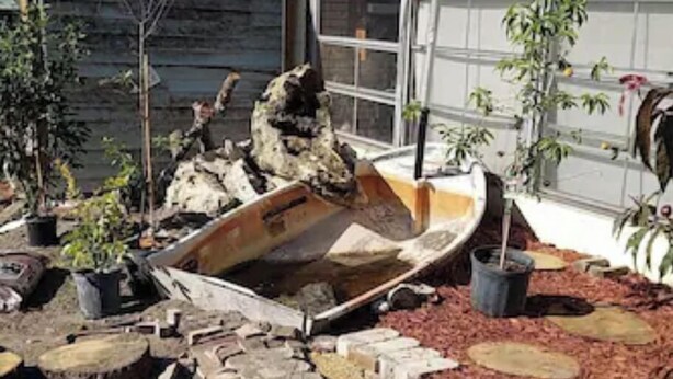 Un jardin avec un bateau en bois, des plantes en pot et un chemin de pierres.