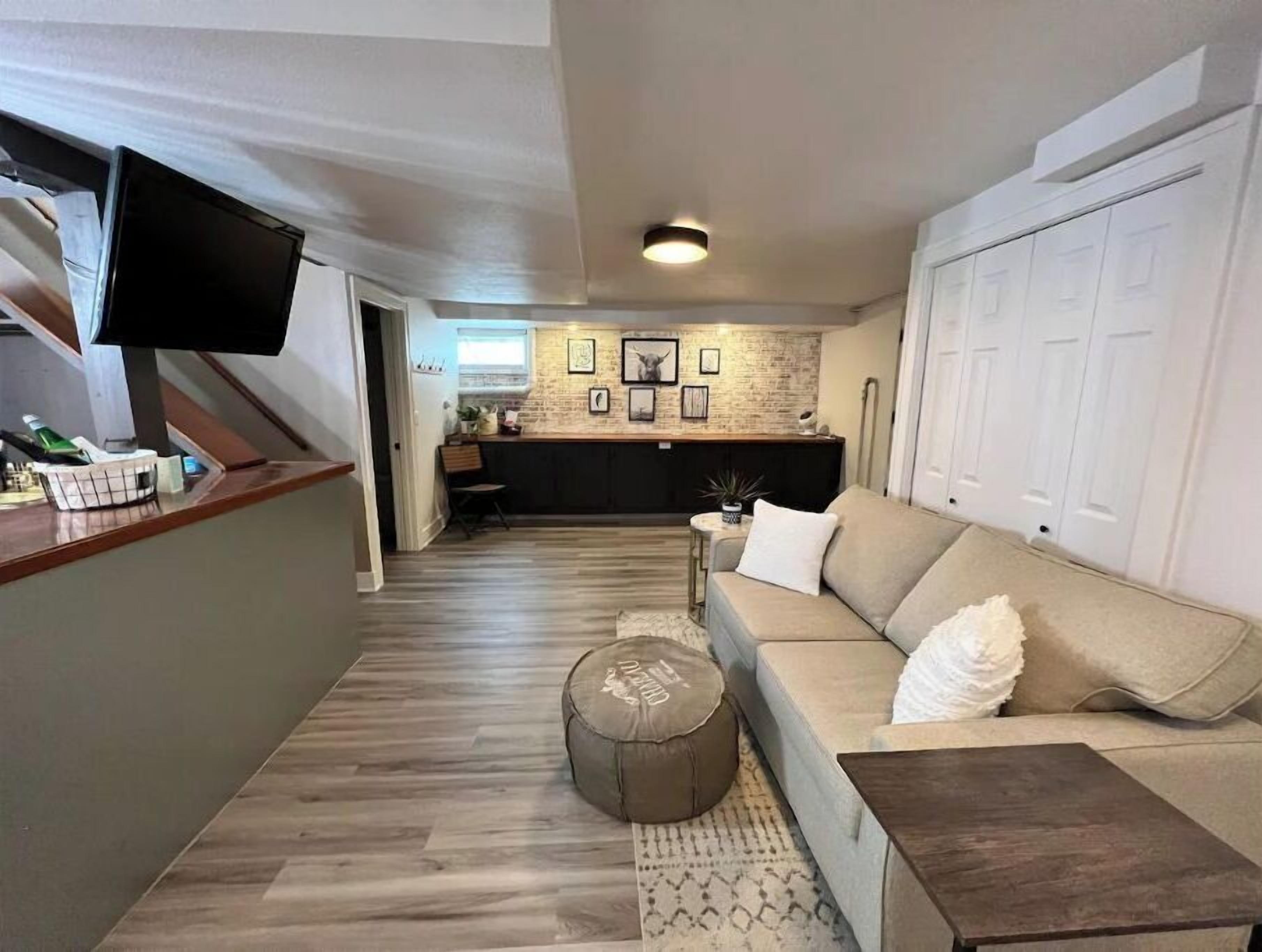 A modern living room with a sofa, ottoman, and coffee table. A kitchen is visible in the background.