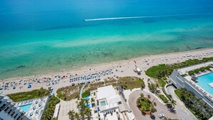 Vista aérea de un resort en la playa con piscina, sombrillas y una vista despejada del océano.