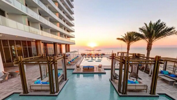 Zona de piscina en la azotea con sillones y vistas al atardecer sobre el océano.