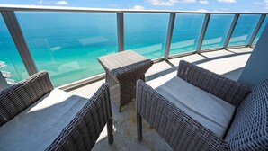 Un balcón con mobiliario de mimbre y barandilla de cristal con vistas al mar azul y despejado.