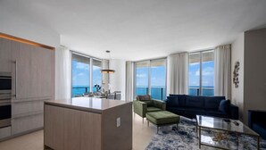 Una sala moderna con un ventanal grande, un sofá, una mesa de centro y una zona de cocina con una isla central.