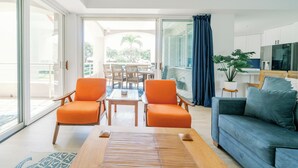 A modern living room with a sofa, two orange armchairs, a wooden coffee table, and a dining area with a table and chairs. - Newly Renovated High-end 1 bedroom, 2 bathroom Wailea Condo close to beach (Kihei)