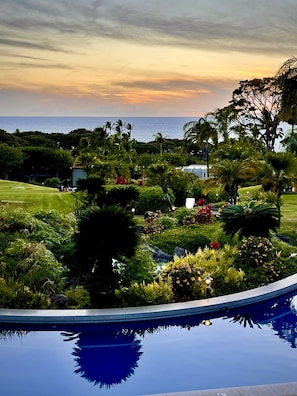 A pool with a view of a landscaped garden and the ocean at sunset. - Newly Renovated High-end 1 bedroom, 2 bathroom Wailea Condo close to beach (Kihei)