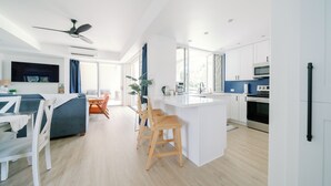 A modern kitchen with white cabinets, a central island, and wooden chairs. - Newly Renovated High-end 1 bedroom, 2 bathroom Wailea Condo close to beach (Kihei)