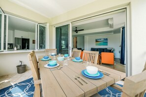 Un coin repas avec une table en bois dressée pour quatre personnes, des assiettes bleues et blanches, et une vue sur le salon à travers une porte ouverte.
