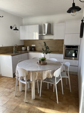Moderni keittiö, jossa on valkoiset kaapit, pyöreä ruokapöytä tuoleineen, sisäänrakennettu uuni ja puinen työtaso.