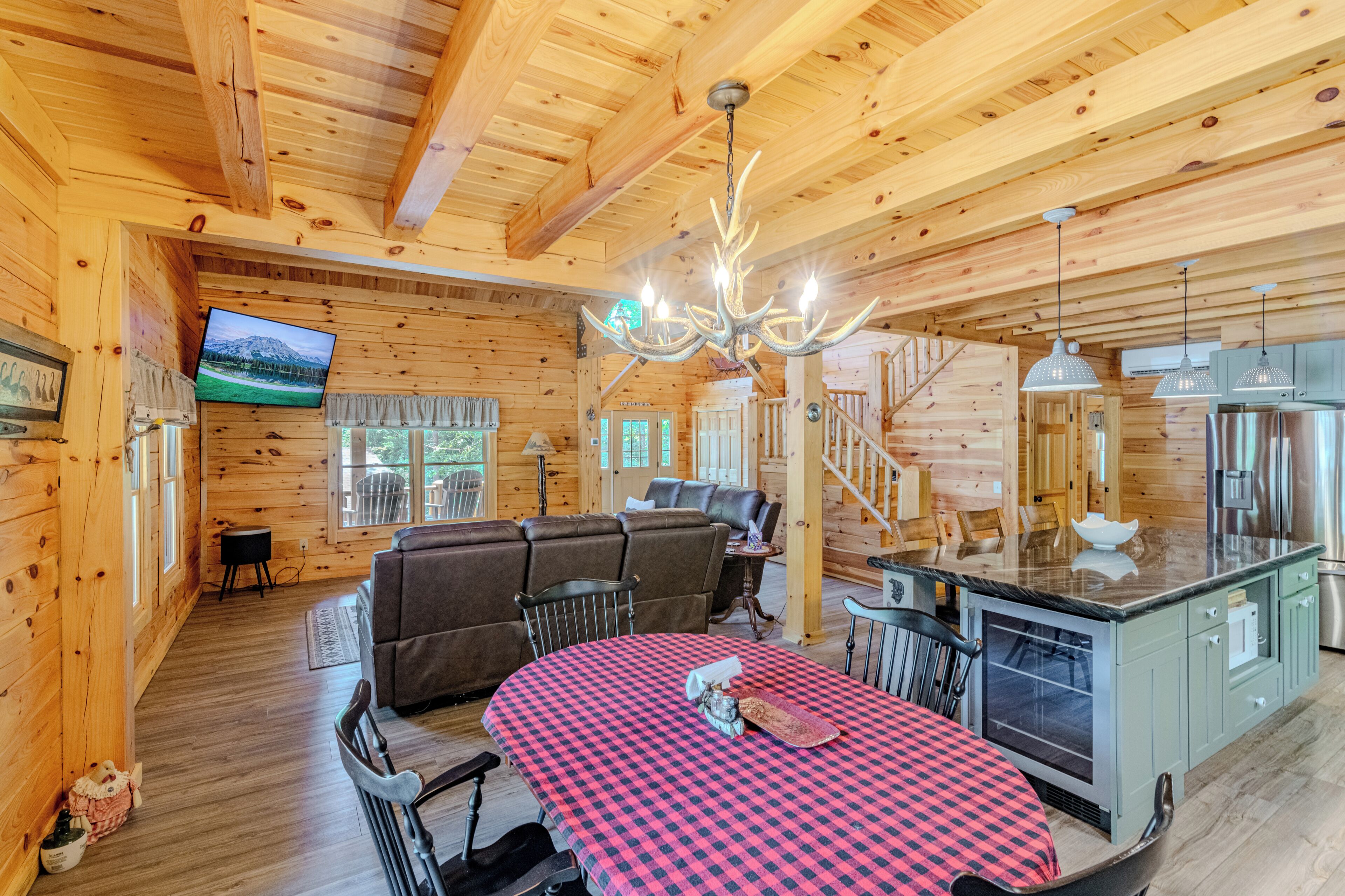 A wooden cabin interior with a dining area, a sofa, a television, and a staircase.