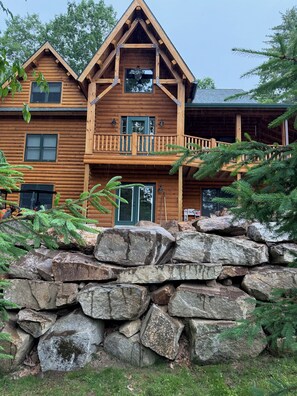 Une cabane en rondins avec des fondations en pierre, un balcon et une grande fenêtre.