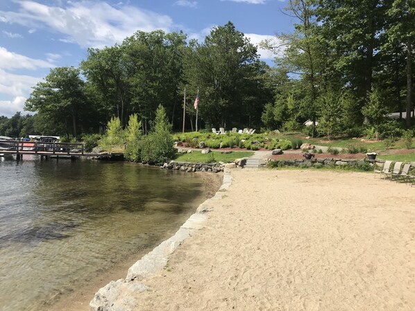Une zone au bord du lac, avec une plage de sable, un quai où sont amarrés des bateaux et une rangée de chaises.