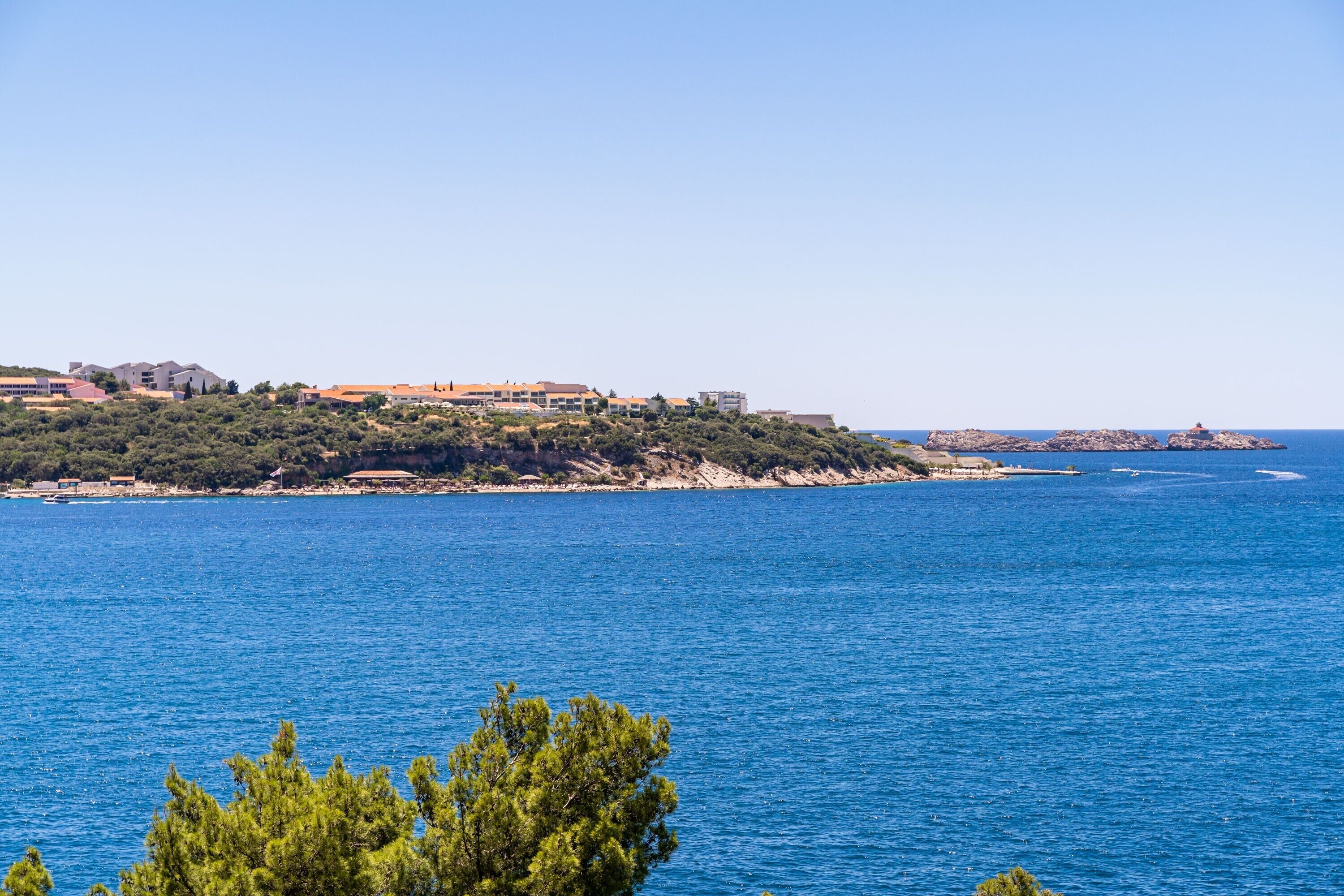 A coastal view with buildings on a hillside and a clear blue sea.