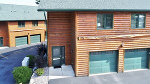 A log cabin with two garage doors, a small porch, and a green roof.