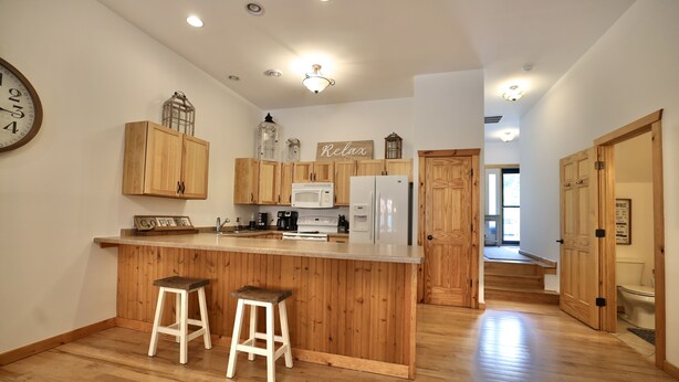 A modern kitchen with wooden cabinets, a central island with stools, and a visible clock on the wall.