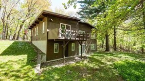 A two-story cabin with a balcony, surrounded by trees.