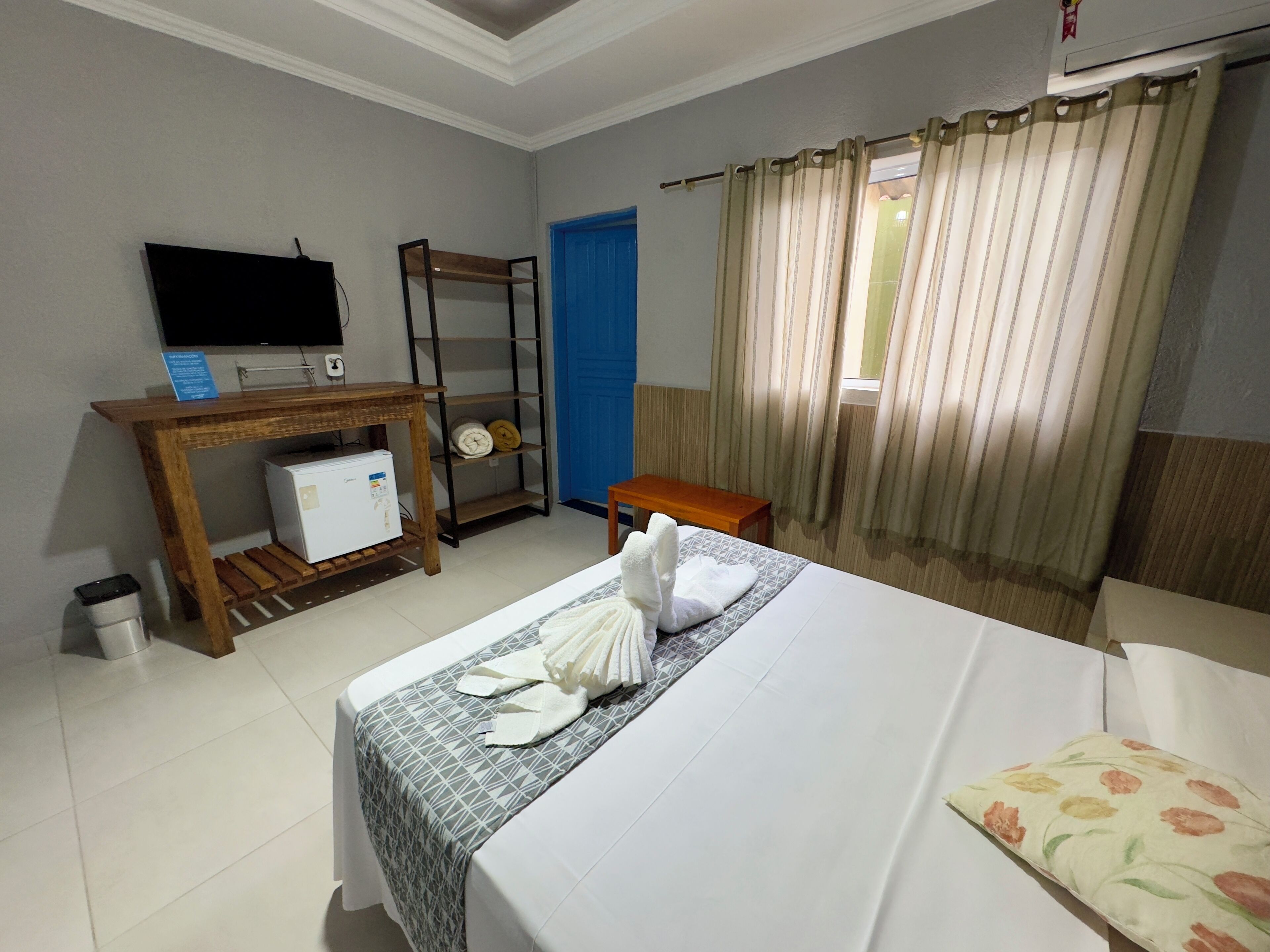 Habitación de hotel con cama, escritorio pequeño con computadora, televisor montado en la pared y ventana con cortinas.