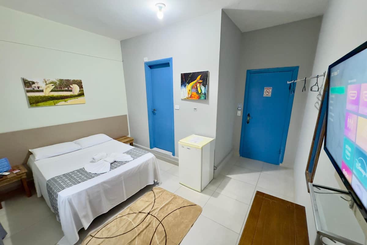A hotel room with a bed, a desk, a chair, a TV, and two blue doors.