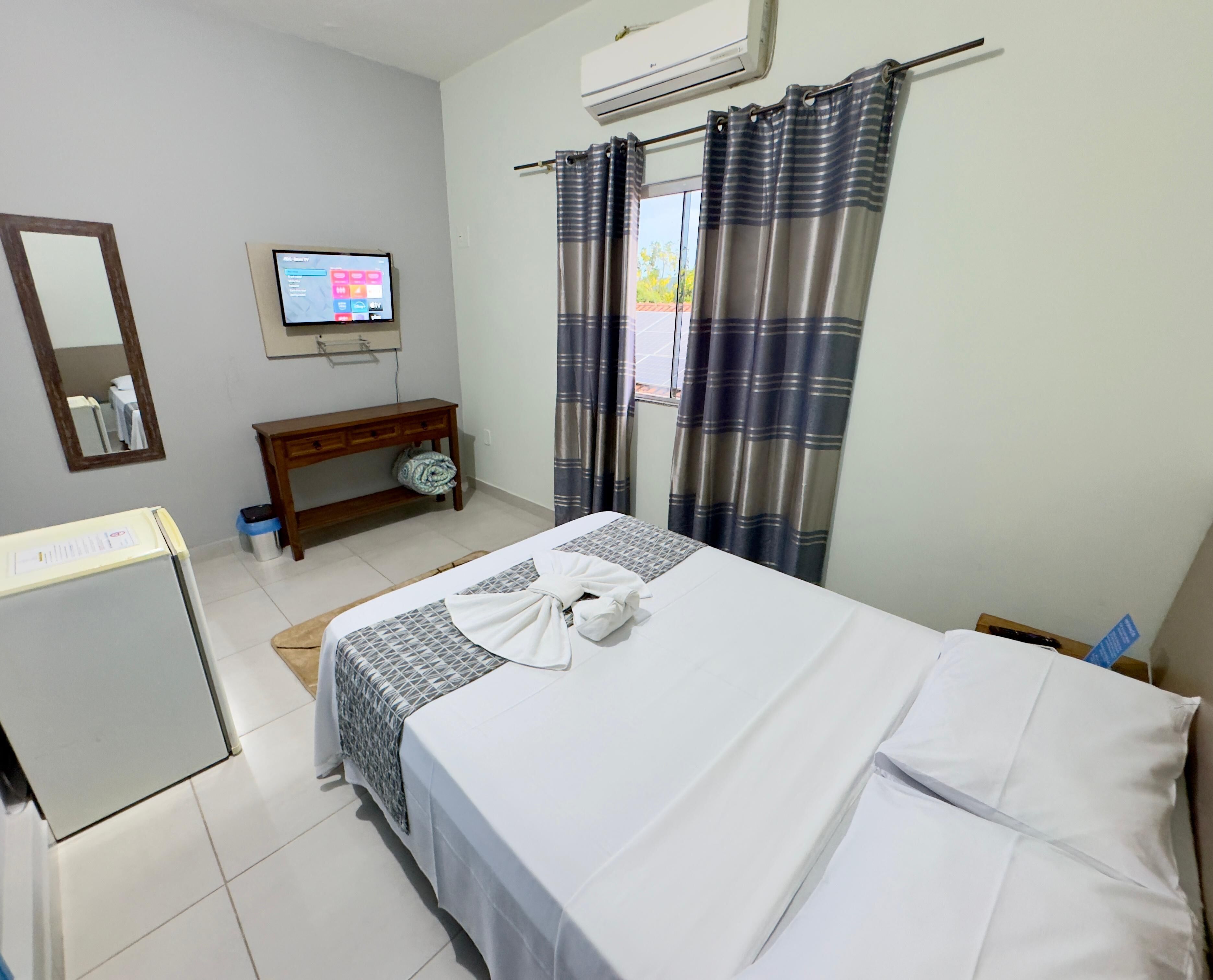 A hotel room with a bed, a TV, a small desk, and a window with curtains.