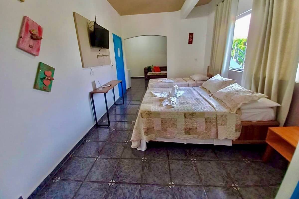A bedroom with a bed, a desk, and a chair. There is a window with curtains and a door.
