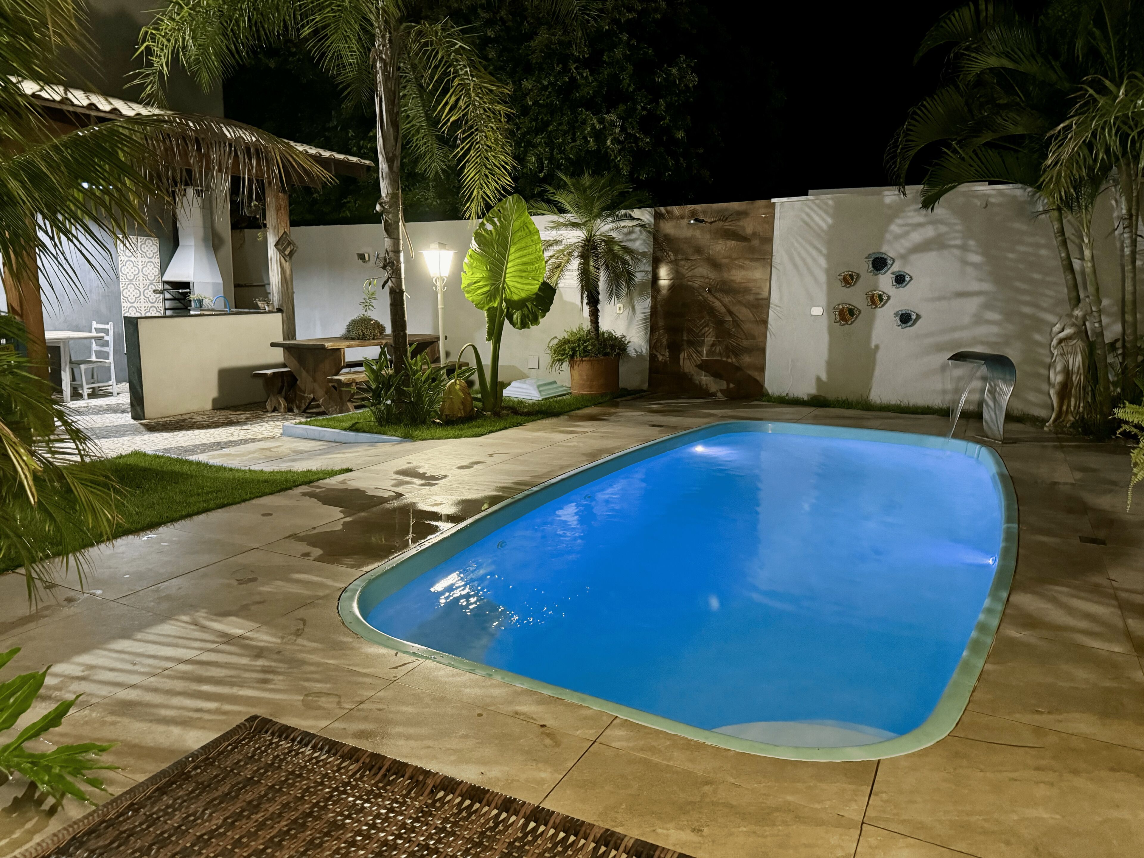 A swimming pool with a tiled deck, surrounded by palm trees and a white wall with decorative elements.