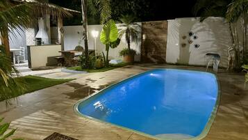 A swimming pool with a tiled deck, surrounded by palm trees and a white wall with decorative elements.